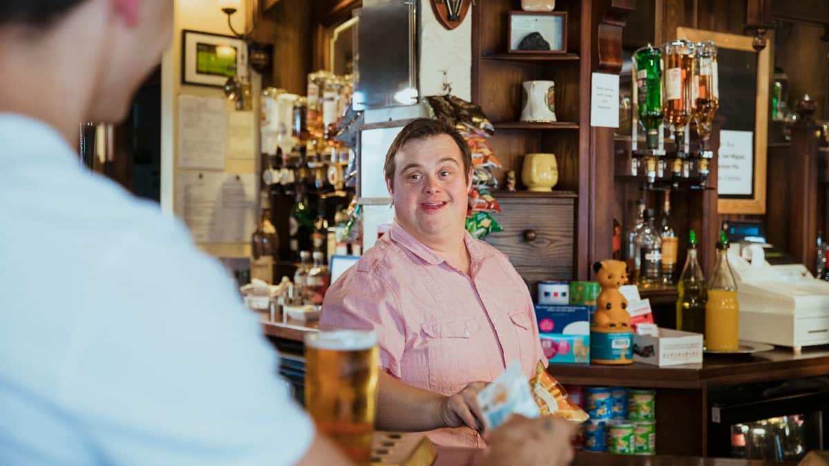 A man with Down's syndrome serves a customer a pint of beer in a pub.