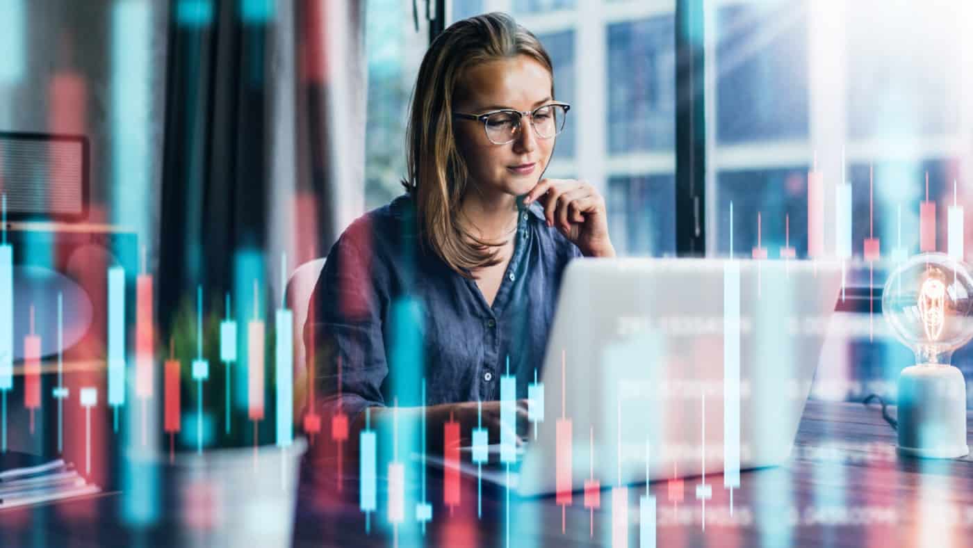 Young woman working at modern office. Technical price graph and indicator, red and green candlestick chart and stock trading computer screen background.