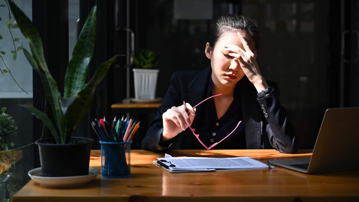 Young Asian woman with head in hands at her desk