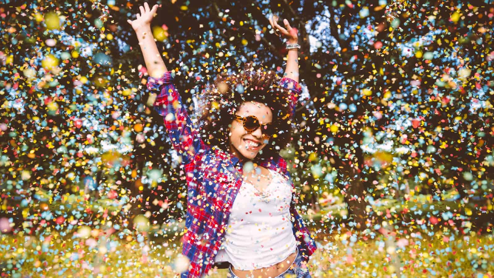 Young mixed-race woman jumping for joy in a park with confetti falling around her