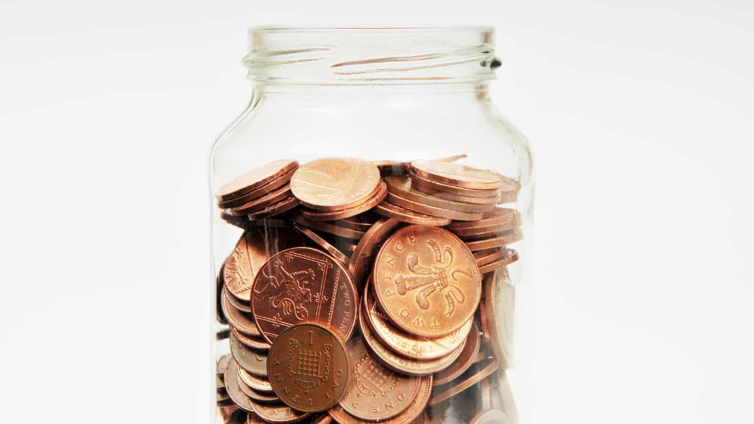 UK coins (1p & 2p) in a savings glass jar against a plain studio background.