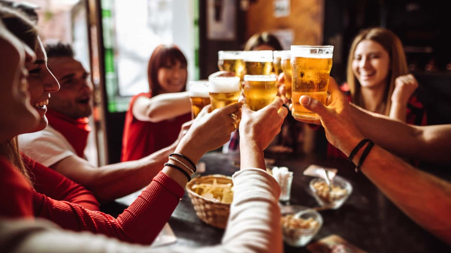 Group of young friends toasting each other with beers in a pub