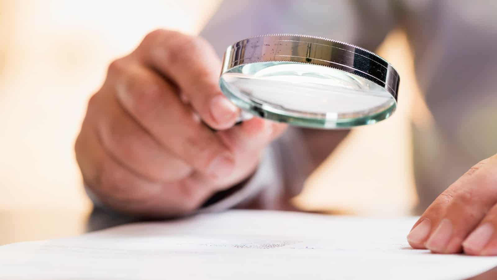 Person holding magnifying glass over important document, reading the small print