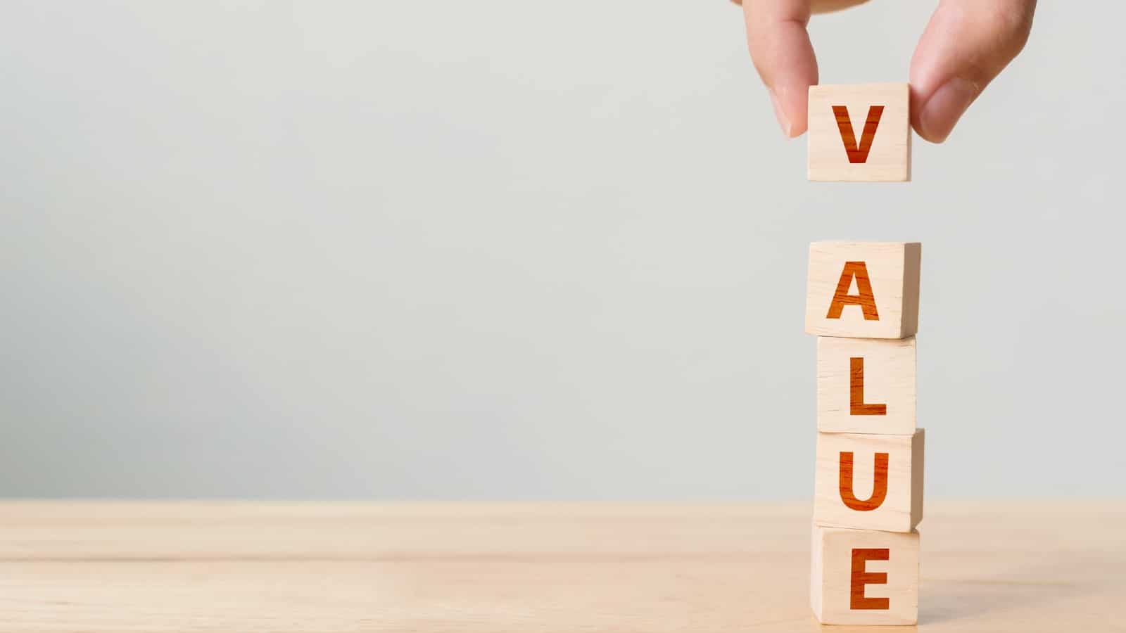 Hand of person putting wood cube block with word VALUE on wooden table