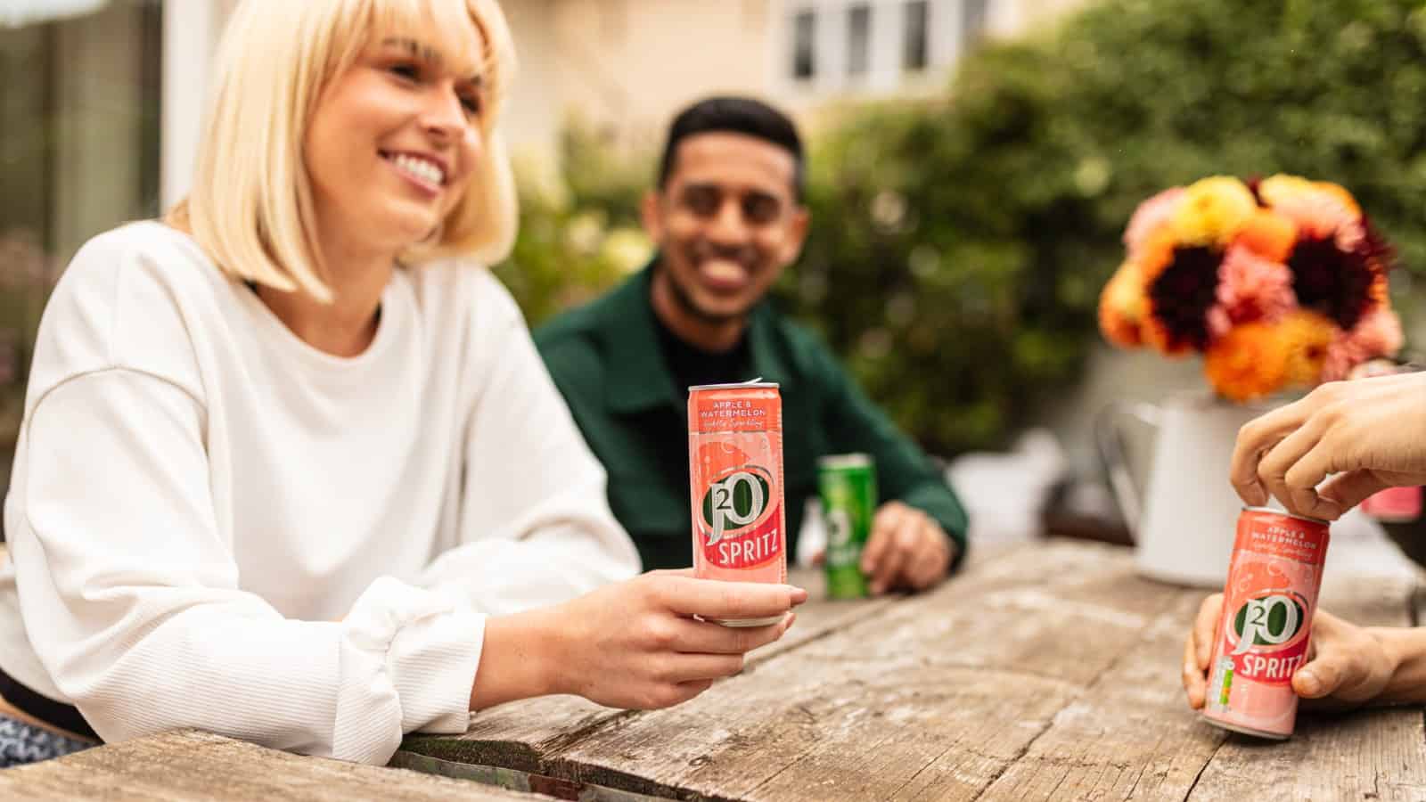 Three young adults drinking cans of J20 Spritz in a pub garden