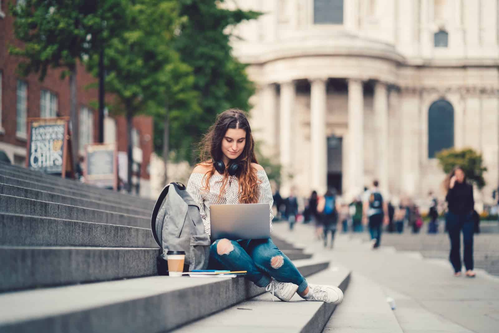 Female student sitting at the steps and using laptop
