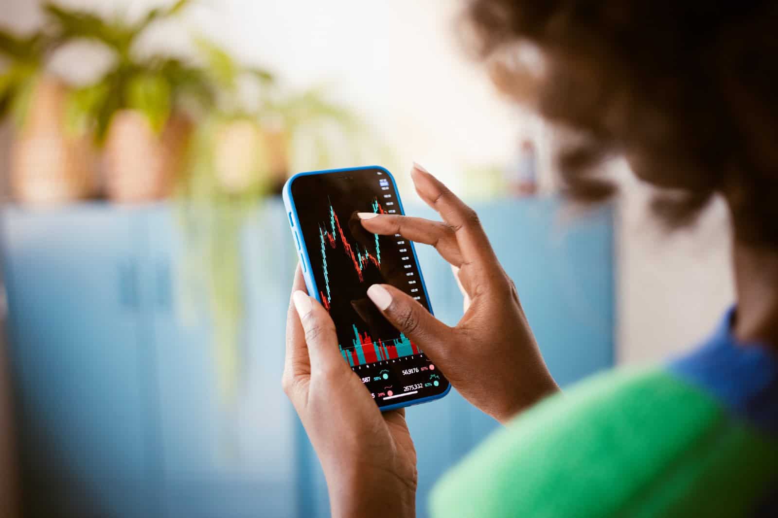 Black woman using smartphone at home, watching stock charts.