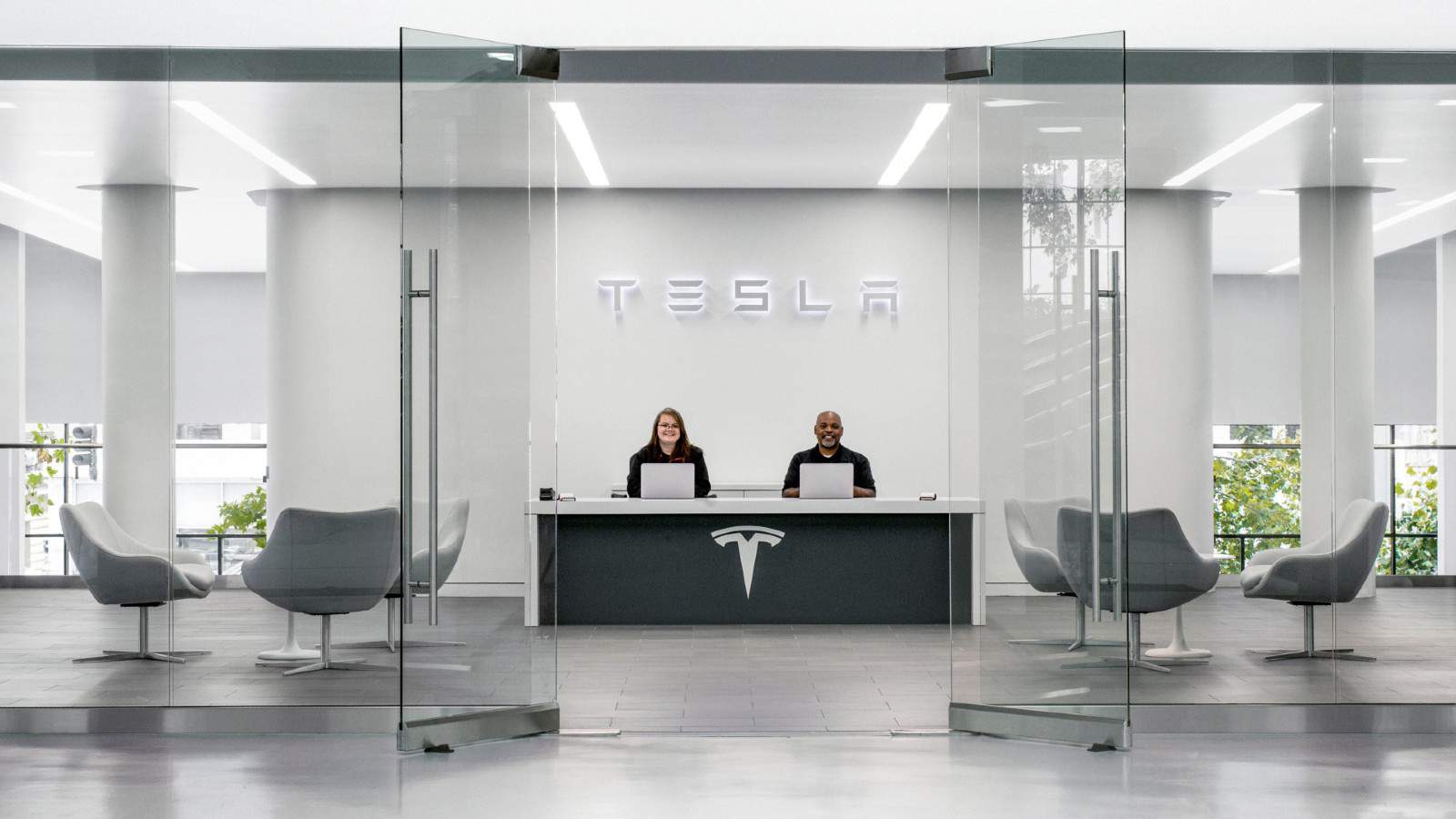 Two employees sat at desk welcoming customer to a Tesla car showroom