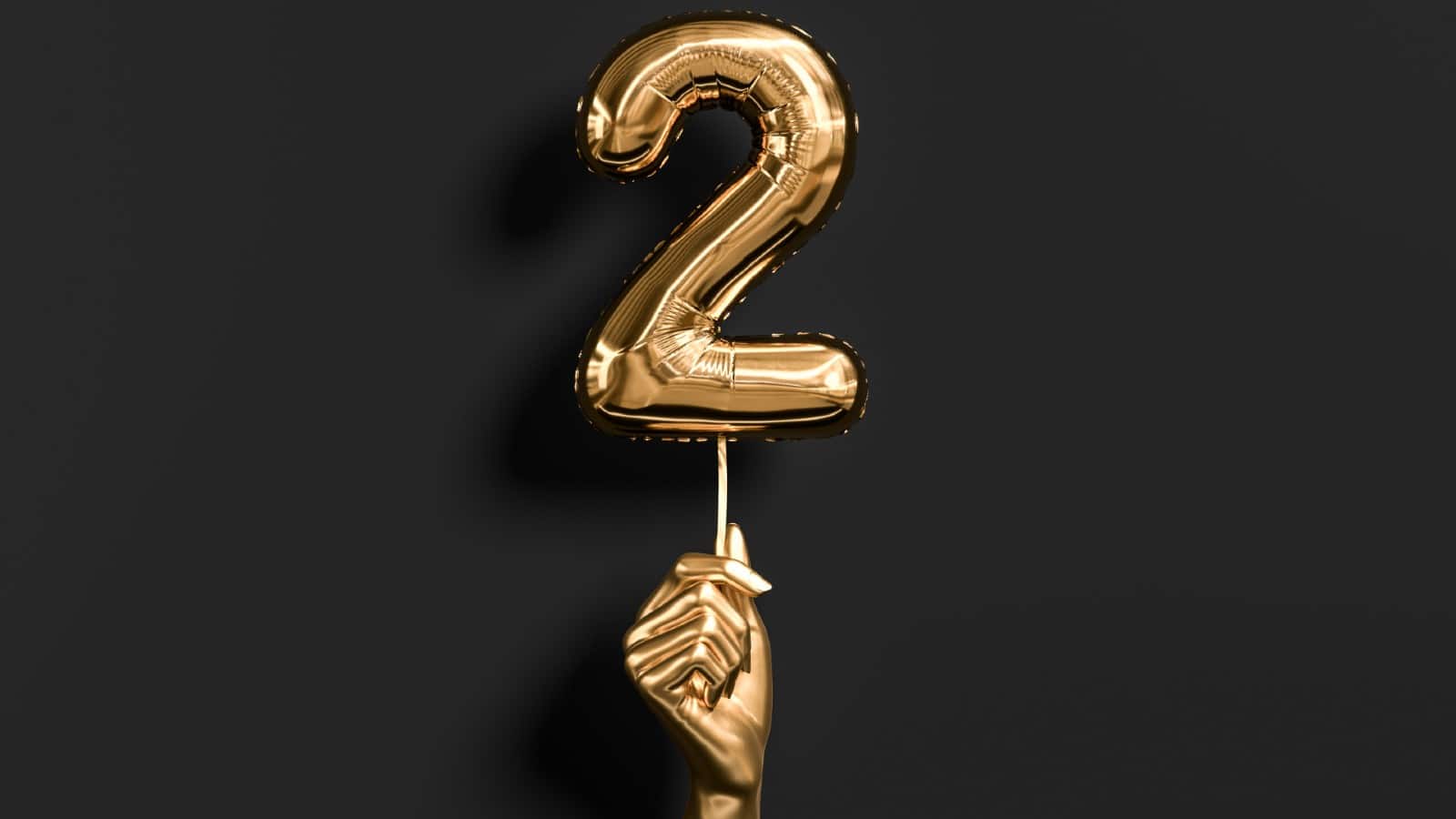 Golden hand holding Number 2 foil balloon.