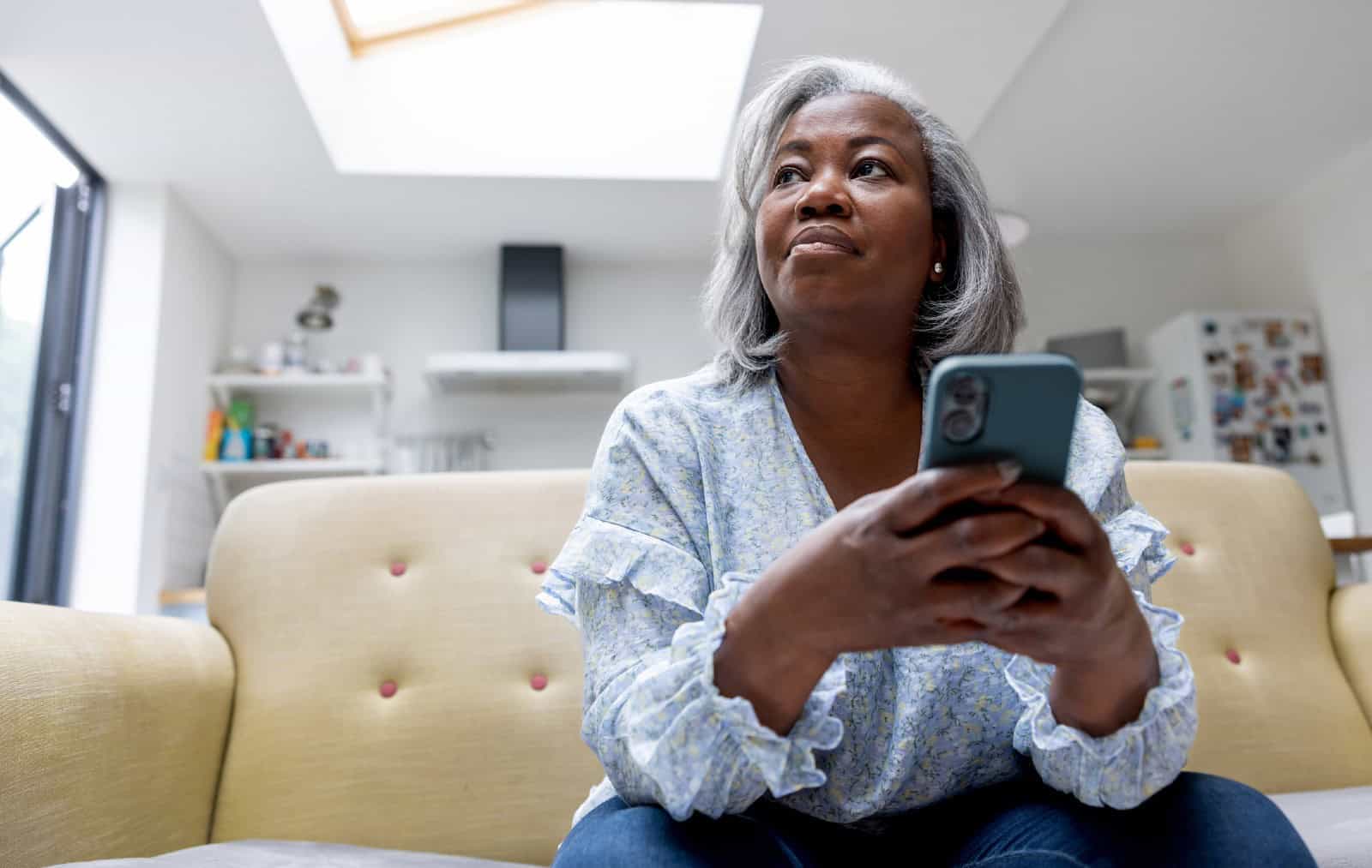 Mature black woman at home texting on her cell phone while sitting on the couch